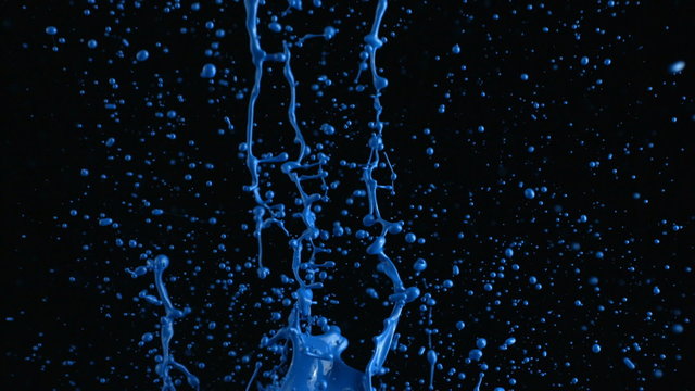 Blue paint splattering on black background, slow motion