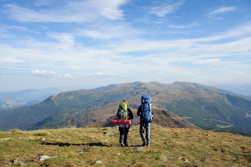 Fototapeta na wymiar Young couple walking together on the mountain summit enjoying beautiful open panoramic view and their hike together. Hiking gear/equipment. Man and woman using trekking sticks.