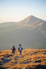 Obraz premium Young couple hikers with their backpacks on walking on mountain plato against beautiful mountain on background. Alternative lifestyle. Cross country hiking.