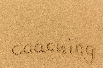 Coaching - inscription on sand beach.