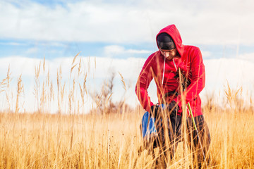 Man hiker standing in the field and putting his water bottle inside a backpack on a background of the blue sky