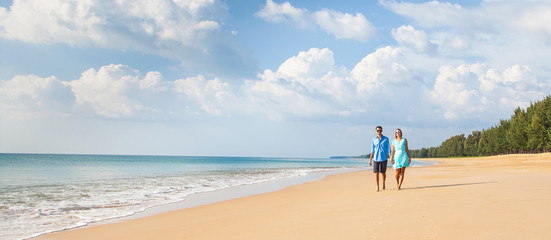 Couple walking on beach. Young happy interracial couple walking on beach smiling holding around each other.  Banner