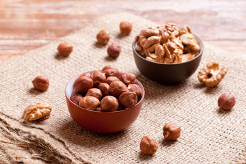 walnuts and hazelnuts in bowls on wooden background