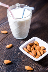 Cup of almond milk with drinking straws and nuts on table