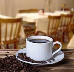 Coffee beans and coffee in white cup on wooden table opposite a
