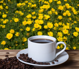 Coffee beans and coffee in white cup on wooden table opposite a