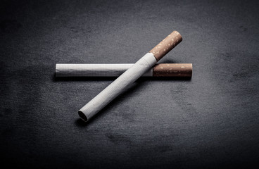 Two cigarettes on a black slate cutting board. Toned