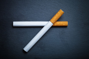 Two cigarettes on a black slate cutting board. Toned