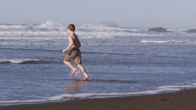 Young boy running in ocean surf, slow motion