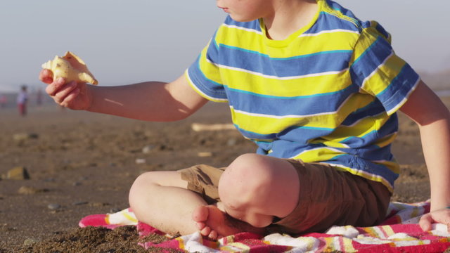 Boy at beach picks up shell and listens