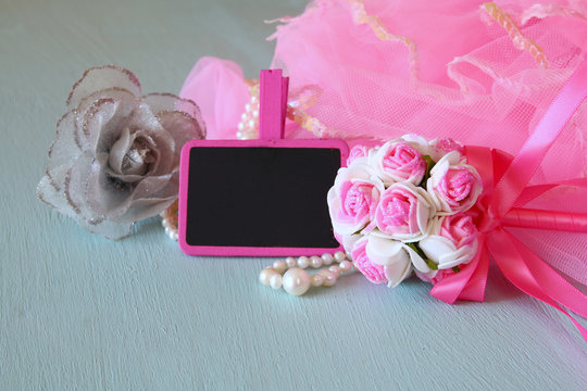 Small girls party outfit: crown and wand flowers next to small empty chalkboard on wooden table. bridesmaid or fairy costume