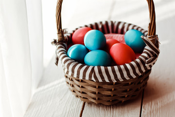 Multicolored Easter eggs in wicker basket on white wooden background