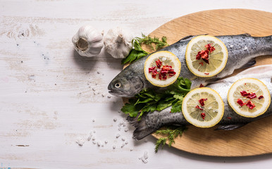 Fish dish cooking with various ingredients. Raw rainbow trout with lemon, garlic ,herbs and spices on cutting board , top view. Healthy food or diet nutrition concept.