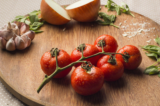 Close-up of fresh tomatoes, garlic, onion and basil on a wooden chopping board 