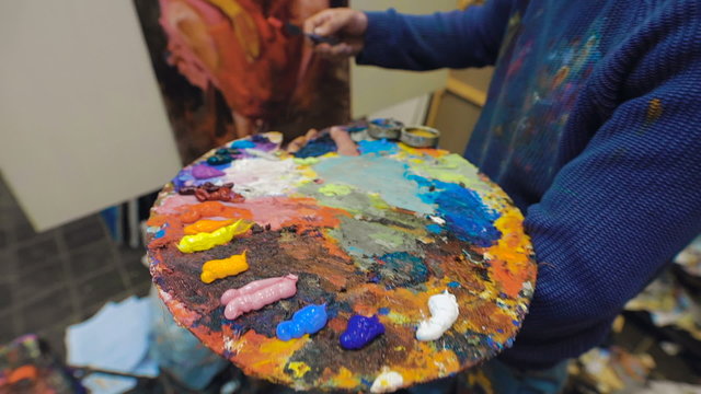 artist paints a picture of oil paint brush in hand with palette 
