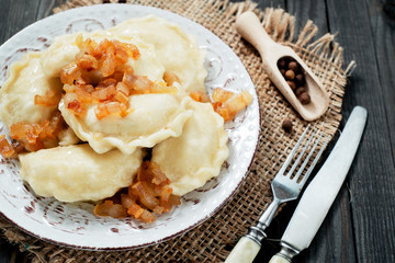 traditional Ukrainian and Russian cuisine , dumplings called varenyky of dough with meat, pepper and fat or salo in a clay plate on a dark wooden background