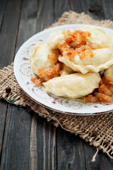 traditional Ukrainian and Russian cuisine , dumplings called varenyky of dough with meat, pepper and fat or salo in a clay plate on a dark wooden background