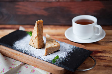 Sweet almond cake with cup of tea on old wooden background with