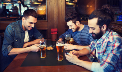 male friends with smartphones drinking beer at bar