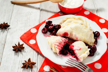 traditional Ukrainian and Russian cuisine , sweet dumplings called varenyky of dough with cherry, sour cream and cinnamon in a clay plate on a white wooden background