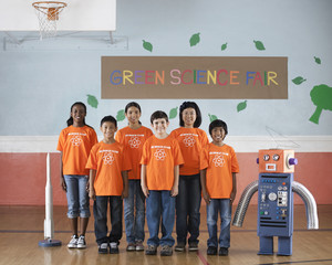 Students in the Science Club standing under the sign Green Science Fair with a rocket and a model robot made from steel tubes and cardboard, 