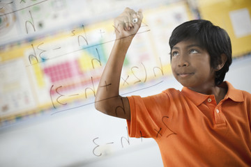 A student writing formula and equations on a clear perspex board, with pens, 