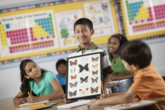 A boy standing in classroom while holding up a frame