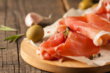 closeup of thin slices of prosciutto with mixed olives and paprika on wooden cutting board