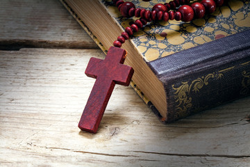 catholic wooden rosary beads with cross on an old book on rustic wood