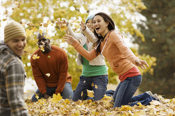 A group of men and women throwing fallen autumn leaves in the air
