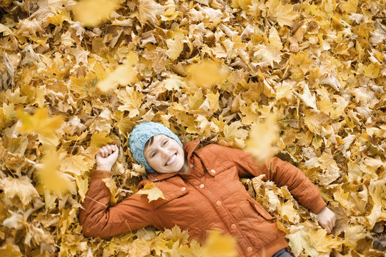 A woman lying on her back on the ground on a covering of autumn leaves, 