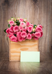 Roses in the box and a greeting card on wooden background