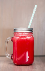 A watermelon smoothie in a mason jar with tube on wooden background
