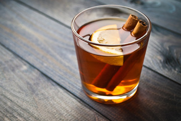Lemon slice and cinnamon sticks in a cup of black tea on wooden background. Close up