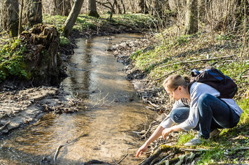 Young woman hiker with backpack by the river in the spring forest