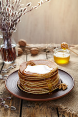 Stack of traditional American pancakes with flowing honey and nuts on vintage wooden table background. Homemade delicious dessert. Rustic style.