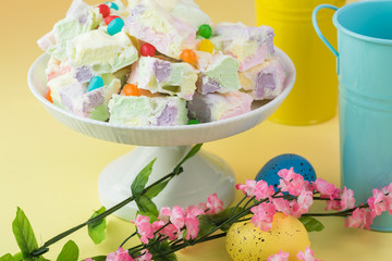 Easter table decoration with homemade fruity marshmallow squares in cake platter, Easter eggs and blossoming brunch.