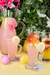 Garden party table with pink lemonade pitcher and glasses and pitcher with strawberry orange blossom punch.