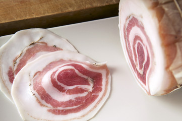 Pancetta classica a fette e intera su piatto bianco