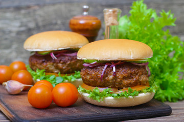 Juicy burgers hamburger with a big beef cutlet, tomato, lettuce and onion on wooden background