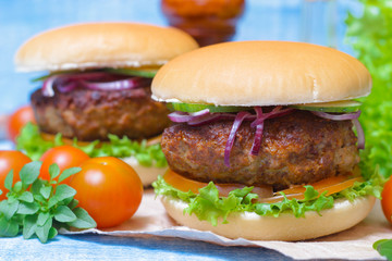 Juicy burgers hamburger with a big beef cutlet, tomato, lettuce and onion on wooden background