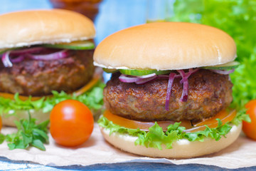 Juicy burgers hamburger with a big beef cutlet, tomato, lettuce and onion on wooden background