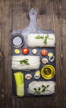 Glass noodles with vegetables and herbs on a cutting board cooking and vegetarian concept on wooden rustic background top view