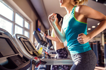 Two fit women running on treadmills in modern gym - obrazy, fototapety, plakaty