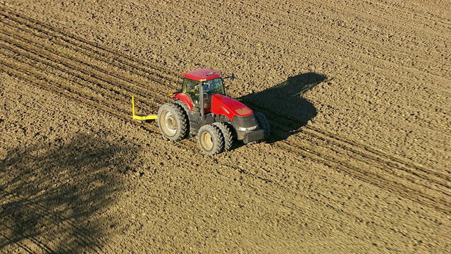 Aerial shot of tractor plowing field, zoom out