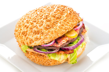 Delicious original american hamburger with grilled beef, bacon and vegetables on white plate, snack or lunch, product photography for restaurant or bistro