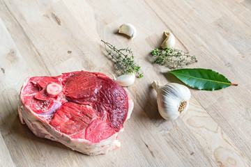 beautiful raw slice of an organic leg of lamb meat with garlic, fresh bay laurel and thyme on a...