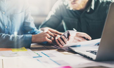 Business meeting concept. Photo young businessmans crew working with new startup project in modern loft. Generic design smartphone holding female hands. Horizontal, film effect