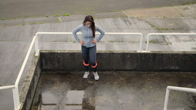Fitness female athlete doing lunges before climbing stairs running for explosive legs and hiit workout. Urban sporty woman training outdoor on rainy day.