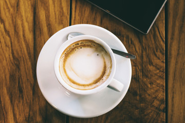 A cup of coffee and smart phone on a woden table in cafe